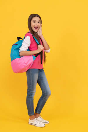 surprised teen school girl with backpack go to study on yellow background, educationの写真素材