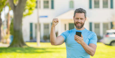 happy mature man standing outdoor at house reading message on smartphone, real estateの写真素材