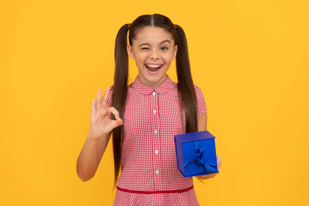 happy kid hold present box on yellow background winking with ok gesture, childrens dayの写真素材