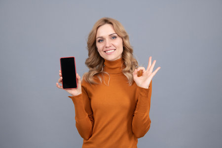 Approved mobile phone. Happy girl show OK sign to smartphone. Approved conceptの写真素材