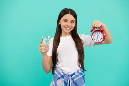 happy kid hold glass of water and clock to stay hydrated and keep daily water balance, thirst.の写真素材
