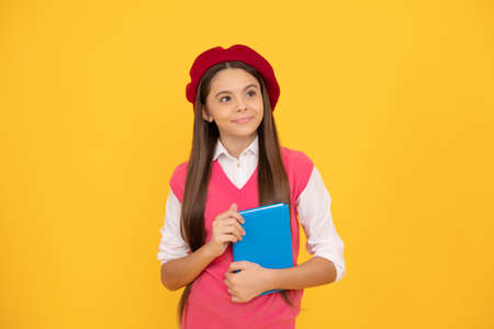 happy teen school girl in french beret hold copybook on yellow background, literatureの写真素材
