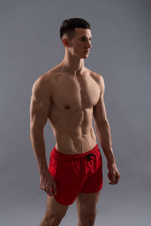 Fit athletic guy with muscular torso in sports shorts grey background, manの写真素材