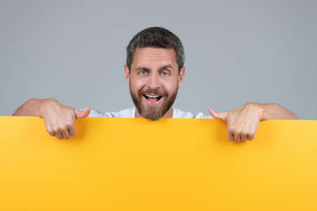 happy mature bearded man behind yellow paper pointing finger on copy scape, announcementの写真素材