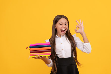 happy teen girl in school uniform hold book stack show ok gesture, self educationの写真素材