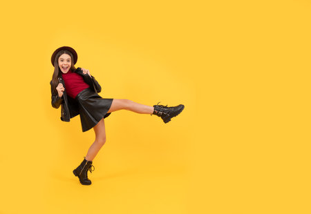 happy teen girl in hat and leather clothes making wide step forward, copy space, having funの写真素材
