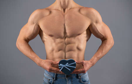 Muscular man with fit six pack abs torso cropped view hold heart-shaped gift box, valentines dayの写真素材