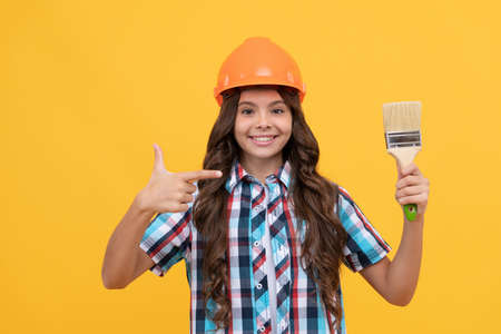 happy child with curly hair in construction helmet pointing finger on painting brush, renovationの写真素材