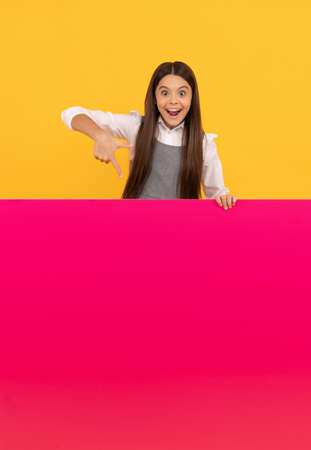 amazed kid pointing finger on blank pink paper sheet for copy space, advertisementの写真素材