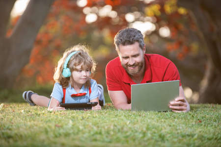happy family of father and son use laptop and headphones in park, modern technology.の写真素材