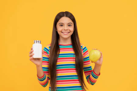 Happy kid hold apple fruit and medicine bottle yellow background, supplementの写真素材