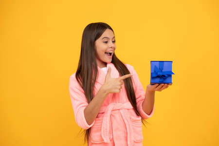 happy teen girl in home terry bathrobe pointing finger on gift or present box, presenting productの写真素材