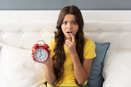 Worried about being late. Anxious girl hold alarm clock. Time late. Oversleeping morningの写真素材
