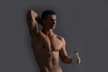 Shirtless man with fit torso hold bath and shower gel grey background, hygieneの写真素材