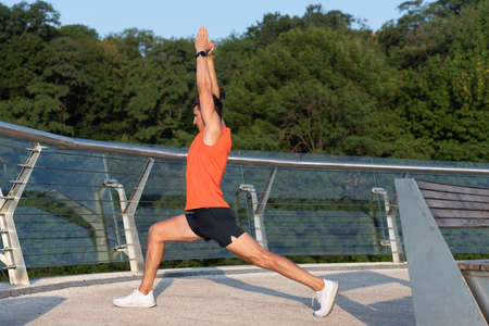 Feel the stretch in your hip. Man do crescent lunge stretch raising arms. Doing yoga or pilates exerciseの写真素材