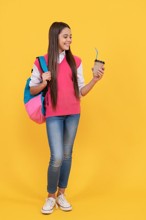 happy teen school girl with backpack drink takeaway cocoa on yellow background, morningの写真素材