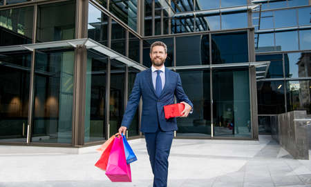 cheerful businessman in formal suit walking with shopping bag presents outdoor, occasion.の写真素材