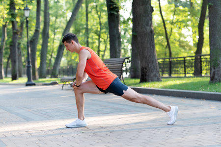 Sportsman hold lunge position doing stretch routine during outdoor athletic workout in park, warmupの写真素材