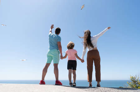 family of mother dad and child boy looking in future holding hands in summer, back view, charityの写真素材