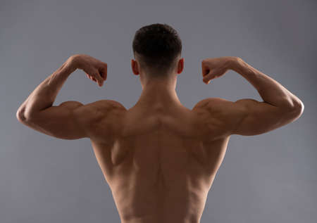 Fit man rear torso flex arm muscle showing biceps triceps grey background, flexingの写真素材