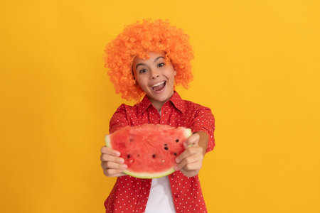 amazed kid in fancy orange hair wig holding fresh ripe water melon slice fruit, organic foodの写真素材