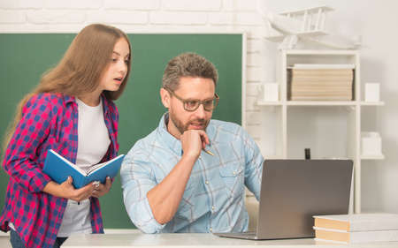 busy teen girl and teacher man in high school with workbook and pc at blackboard, education onlineの写真素材