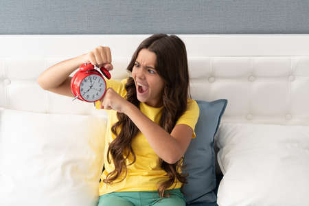 Her alarm clock hadnt gone off. Girl overslept screaming in panic. Shouting child hold alarm clock. Oversleeping. Morning timeの写真素材