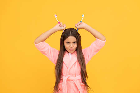 unhappy teen girl in home terry bathrobe hold toothbrush as devils horns, bathroom fun