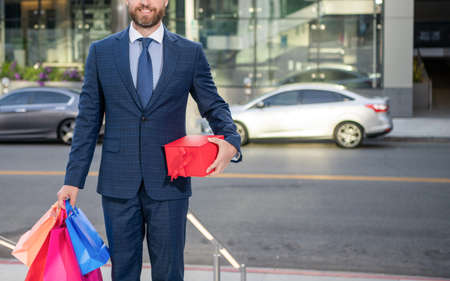 cropped entrepreneur in suit with shopping bags gifts walk outside the office, business reward.の写真素材