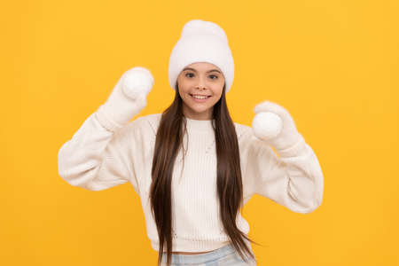 happy child in winter hat and gloves hold snowballs on yellow background, winterの写真素材