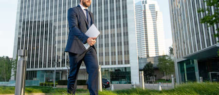 cropped businessman in suit walking with laptop outside the office, agile business