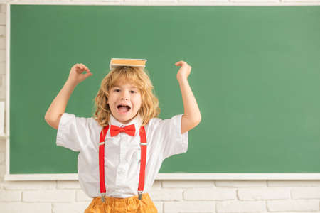 cheerful kid boy in bow tie in school classrrom with book, copy space, back to school