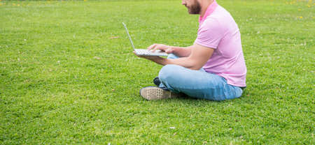 cropped businessman using laptop for blogging on green grass, copy space, network administrator