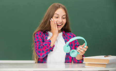 surprised teen girl hold modern headphones in high school at blackboard, school