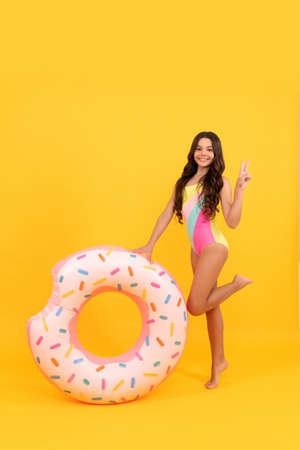 happy beach kid in swimsuit with doughnut inflatable ring on yellow background, swimwear.の写真素材