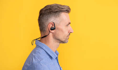 profile of mature man in modern wireless earphones on yellow background, technologyの写真素材
