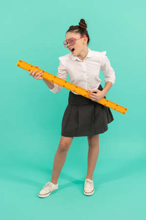 glad teen girl wear uniform and glasses holding mathematics ruler on blue background, measurementの写真素材