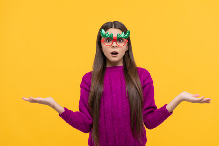 confused teen girl wear party glaasses choosing on yellow background, christmasの写真素材