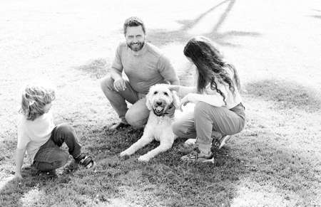 father mother and child on green park grass. friendly family with pet.