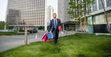 happy man in formalwear with shopping bags and present box walk outside the office, mens day.の写真素材