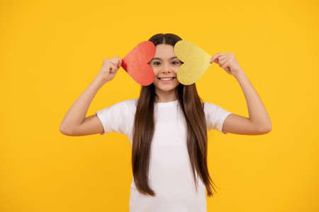 cheerful teen girl holding valentines heart on yellow background, sweetheartの写真素材