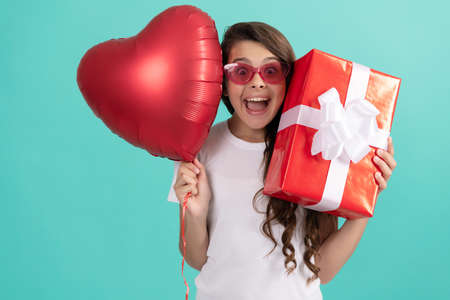 fashionable teen girl in sunglasses hold giftbox and heart balloon. love gift. surprised kidの写真素材