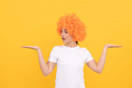 amazed funny girl with fancy look wearing orange hair wig presenting product, copy space, choice.の写真素材