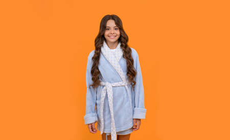 Happy girl child smiling in blue towelling bathrobe orange background, homewearの写真素材