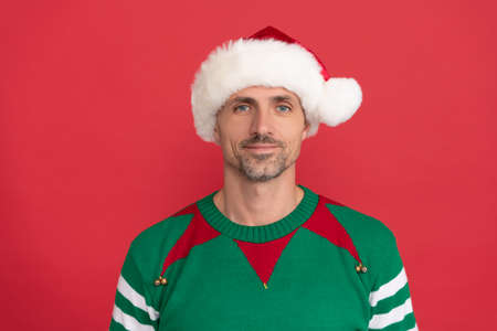 happy man in elf costume. xmas guy in santa claus hat on red background. happy new year.の写真素材