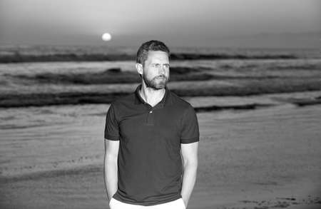 bearded handsome man in summer shirt on beach with sunset over sea, romantic view