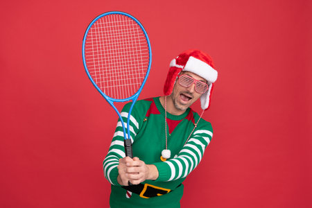 amazed man in elf costume and santa claus hat. xmas guy hold tennis rocketの写真素材