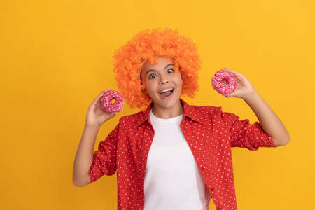 glad teen girl in fancy orange hair wig hold sweet baked doughnut dessert, dental careの写真素材