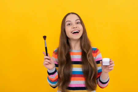 Happy kid apply cosmetics with foundation brush yellow background, makeup.の写真素材