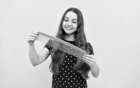 happy kid brushing long hair with comb on yellow background, haircareの写真素材